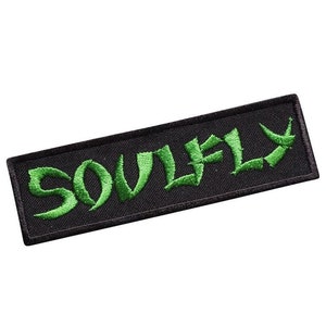 Puede incluir: Parche bordado negro con la palabra "SOULFLY" en letras verdes.