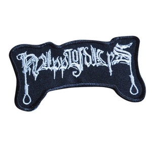 Puede incluir: Parche bordado negro con el texto blanco "Noosegoat" en fuente gótica. El parche tiene forma de nudo corredizo en la parte inferior.