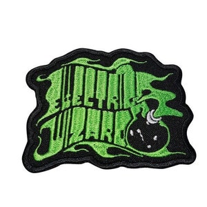 Puede incluir: Parche bordado con las palabras "Electric Wizard" en letras verdes brillantes y estilizadas. El parche tiene un borde negro y presenta un gráfico de bomba verde estilizada. El diseño tiene una estética grunge.