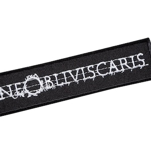 Könnte beinhalten: Schwarzer gestickter Aufnäher mit weißem Text, der "NE OBLIVISCARIS" lautet.