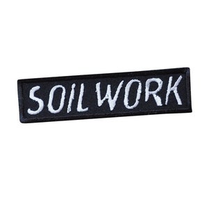 Op de afbeelding: Zwarte geborduurde patch met witte tekst die "SOILWORK" luidt.