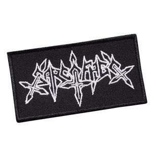 Może przedstawiać: Czarna prostokątna naszywka z białym haftowanym napisem „ARSMEHER”. Tekst ma gotycki, stylizowany krój. Naszywka jest prawdopodobnie przeznaczona na odzież lub akcesoria.