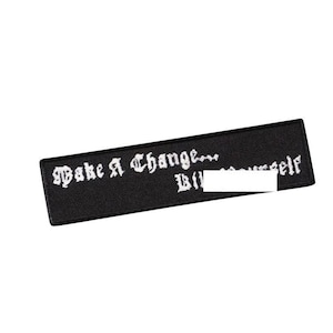 Op de afbeelding: Zwarte geborduurde patch met witte tekst die "Make A Change... Believe In Yourself" luidt.