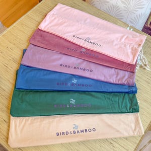 May include: A stack of six colorful fabric pouches in shades of pink, burgundy, lavender, blue, green, and beige. Each pouch has a drawstring closure and the text "BIRD & BAMBOO" printed on it in a contrasting color.