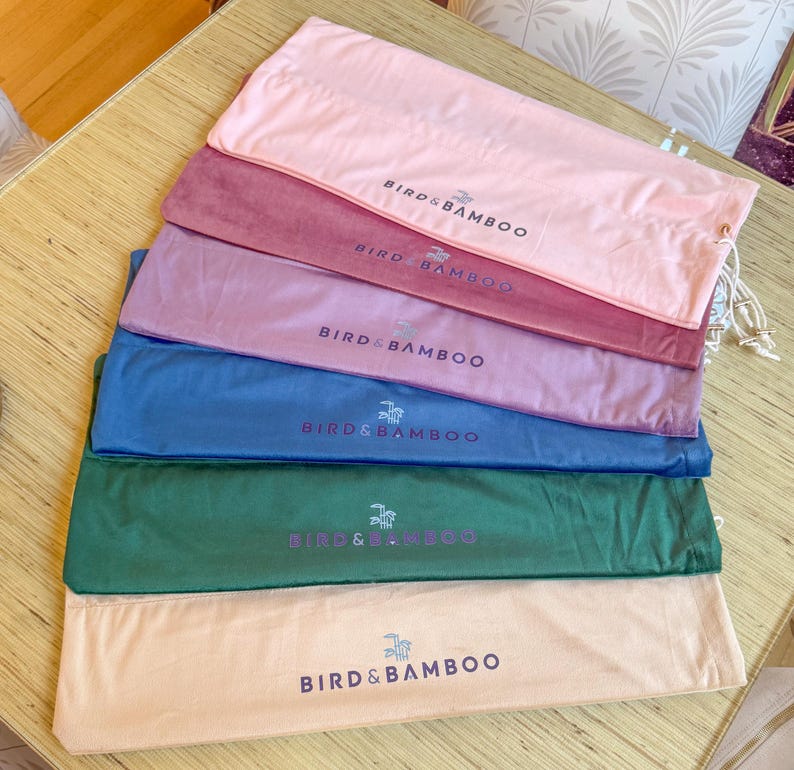 May include: A stack of six colorful fabric pouches in shades of pink, burgundy, lavender, blue, green, and beige. Each pouch has a drawstring closure and the text "BIRD & BAMBOO" printed on it in a contrasting color.