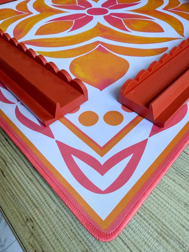 May include: An orange and white patterned play mat with two orange plastic track pieces. The mat features a geometric design with orange, pink, and white colors. The track pieces have a scalloped edge.
