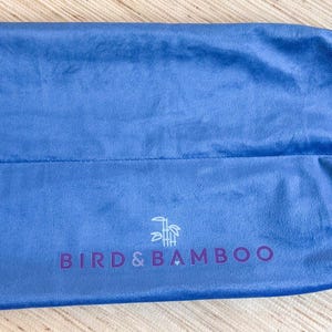 May include: A blue drawstring bag made of soft fabric. The bag has a white drawstring closure and the text "BIRD & BAMBOO" in purple. A logo of a bird and bamboo is above the text.