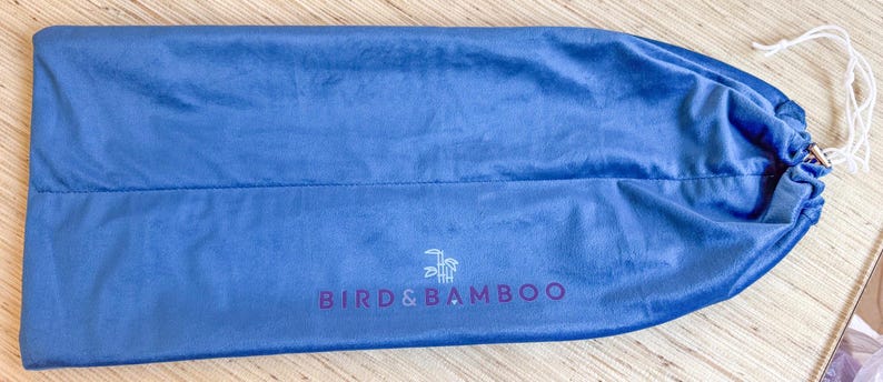 May include: A blue drawstring bag made of soft fabric. The bag has a white drawstring closure and the text "BIRD & BAMBOO" in purple. A logo of a bird and bamboo is above the text.