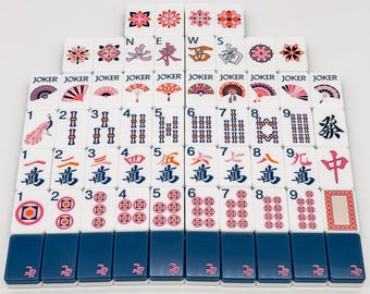 May include: A set of white mahjong tiles arranged in rows, featuring colourful floral designs, fans, numbers, Chinese characters, and the word JOKER. The bottom row consists of solid dark blue tiles with a small pink bamboo graphic at the base.