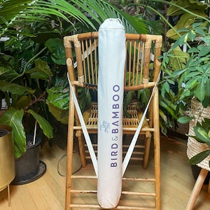 May include: A white canvas bag with the text "BIRD & BAMBOO" printed on it in purple. The bag is hanging on a wooden chair.