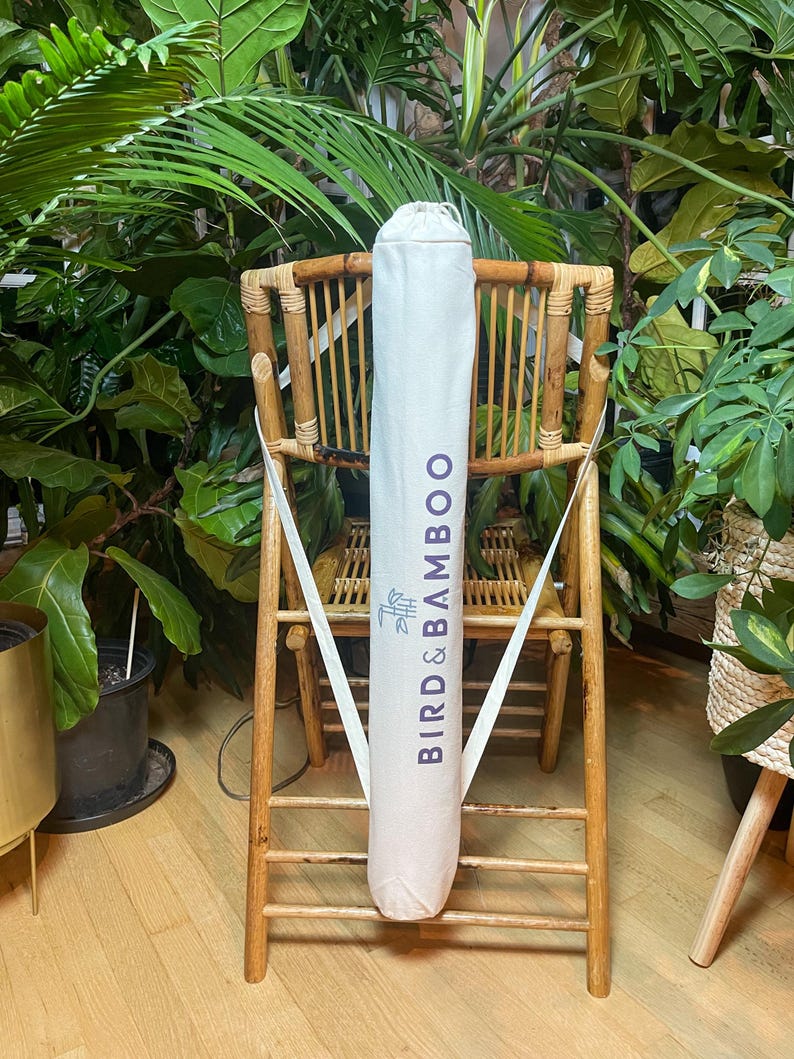 May include: A white canvas bag with the text "BIRD & BAMBOO" printed on it in purple. The bag is hanging on a wooden chair.