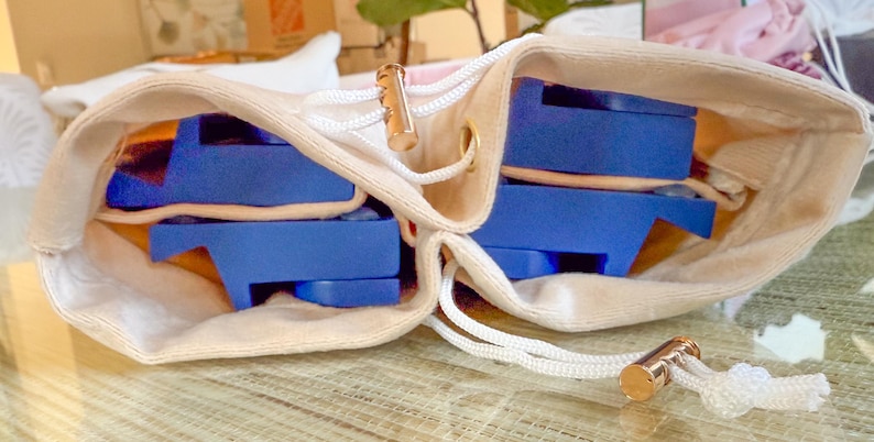 May include: A beige drawstring bag with a gold-colored metal accent and white cord. Inside the bag are several blue objects. The bag is open, revealing the contents. The objects appear to be some type of storage or organizational tool.