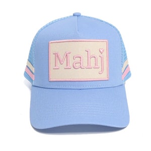 May include: A light blue trucker hat with a pink and white striped band around the crown. The hat has a beige patch with the word "Mahj" in pink letters and a small pink heart.