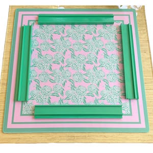 May include: A green glass cutting board with a pink floral pattern. The board has a green frame around the edge.