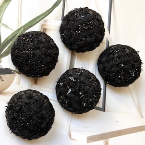 May include: Five round, black tweed buttons with a textured surface and silver metallic accents. The buttons are arranged on a white surface, showcasing their detailed weave and design. These buttons are ideal for sewing and craft projects.