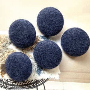 以下が含まれることがあります： 模様のある表面に配置された、濃いネイビーブルーのフェルトボールが5つ。ボールは丸く、質感のある外観をしています。フェルトボールは単色で、手作りのようです。ボールは白と茶色の表面に置かれています。