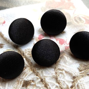 Może przedstawiać: Pięć czarnych guzików satynowych, każdy z gładką, zaokrągloną powierzchnią. Guziki są ułożone w półkole na białym tle z tkaniny.