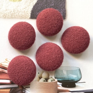 Peut inclure: Cinq objets sphériques avec une surface en feutre rouge foncé texturée, disposés en groupe. Chaque sphère présente un aspect dense et fibreux caractéristique de la laine. Les objets sont uniformes en forme et en couleur, offrant un aspect cohérent.