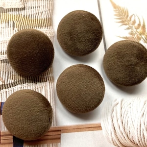 May include: Five brown velvet buttons, each about 1 inch in diameter. The buttons are arranged in a semi-circle on a white surface.