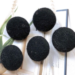 Peut inclure: Un ensemble de quatre boutons noirs circulaires avec une surface texturée et duveteuse. Chaque bouton présente une forme arrondie en dôme avec un aspect doux et fibreux, uniforme en couleur et en taille, conçu pour être fixé sur des vêtements.