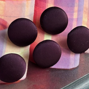 Peut inclure: Cinq boutons ronds en tissu de couleur violet foncé. Les boutons sont légèrement bombés au centre.