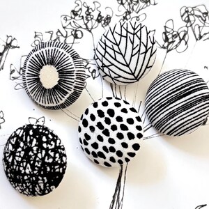 May include: Five circular fabric-covered buttons featuring distinct black and white patterns. The designs include a radial sunburst, a branching leaf motif, horizontal stripes, a dense black speckled pattern, and a textured black and white crackle print.