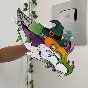 May include: A vibrant, cartoon dragon head with a witch's hat. The dragon is decorated with white, purple, orange, and green, and has a spiderweb pattern. The witch's hat is green with a gold buckle.