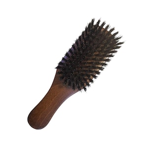 Pode incluir: Uma escova de cabelo de madeira com cerdas de javali naturais. A escova tem uma alça de madeira marrom escura e uma forma oval arredondada.