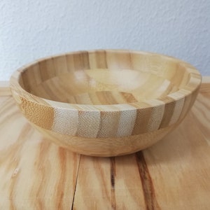 Pode incluir: Uma tigela de madeira natural feita de bambu de cor castanho claro. A tigela é redonda e tem uma superfície lisa.