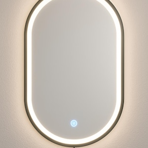 May include: Oval illuminated mirror with a black frame. The mirror features a bright, white LED light outlining the oval shape. A small, blue-lit power button is at the bottom. A black power cord extends downwards.