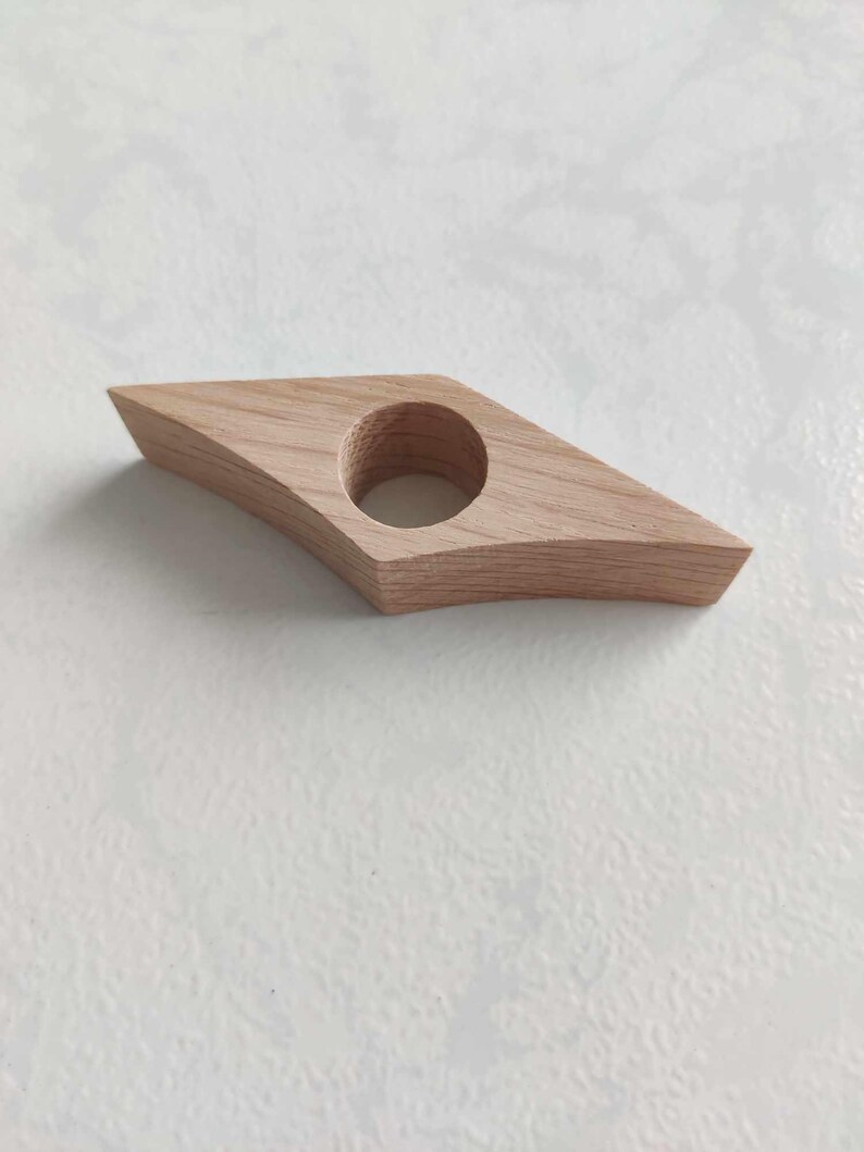 Peut inclure: Un marque-page en bois en forme de diamant avec un trou rond au centre. Le marque-page est en bois brun clair.