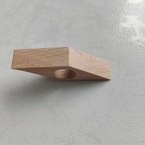 Peut inclure: Un porte-bague en bois brun clair avec une ouverture circulaire au centre. Le porte-bague est en forme de triangle aux bords arrondis.