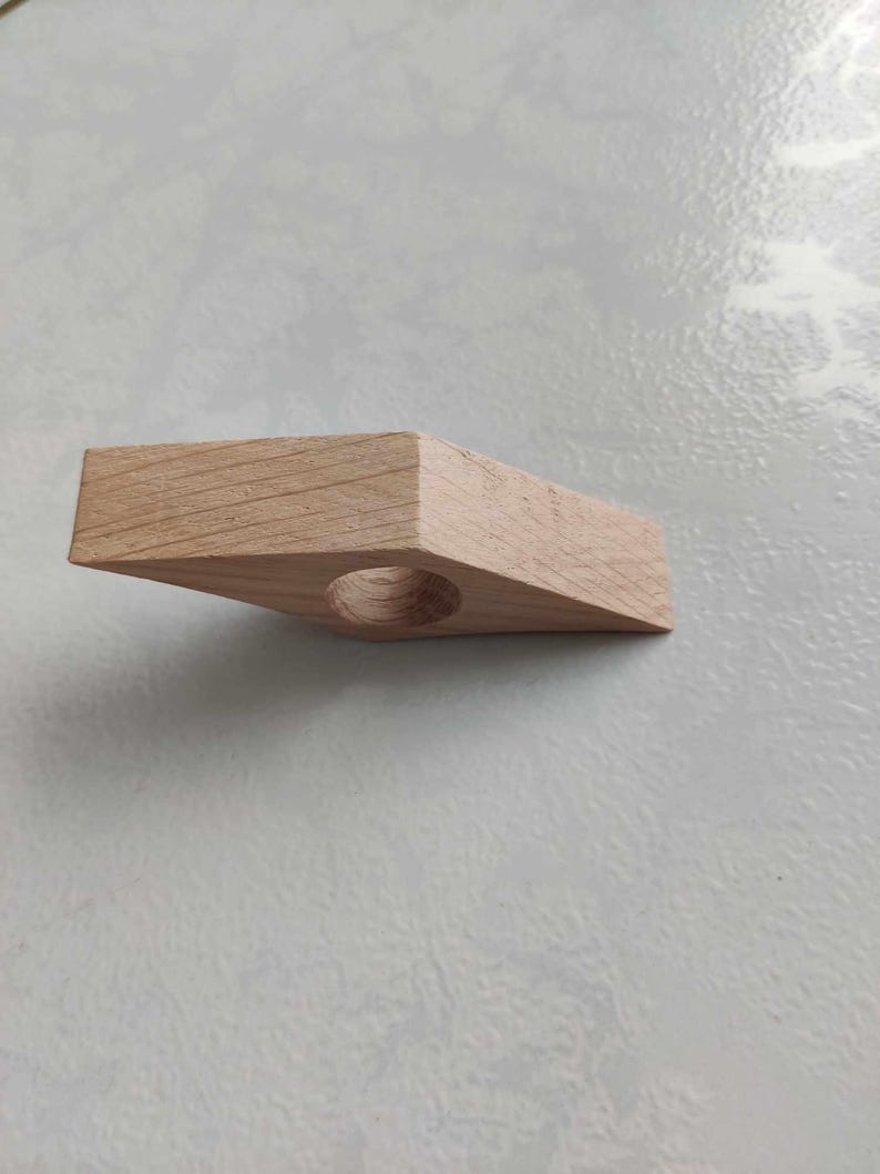 Peut inclure: Un porte-bague en bois brun clair avec une ouverture circulaire au centre. Le porte-bague est en forme de triangle aux bords arrondis.
