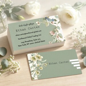 May include: A stack of rectangular business cards and a single card featuring a sage green background with a floral illustration. The text reads Ethan Carter, 616-648-9890, ethan.carter@northwood-global.com, Northwood Global Trading LLC, 1245 Broadway, Suite 310, New York, NY 10001, United States.