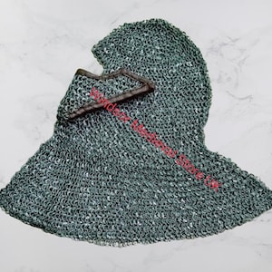 Puede incluir: Una cota de malla gris con una solapa de cuero marrón. La cota de malla es un tipo de casco medieval que cubre la cabeza y el cuello.