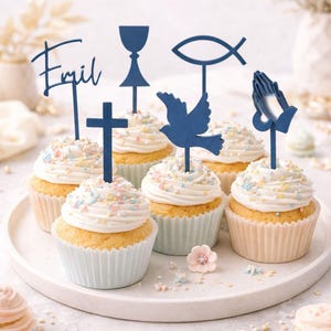 Könnte beinhalten: Cupcakes mit weißem Zuckerguss und bunten Streuseln, gekrönt mit blauen religiösen Symbolen und dem Namen "Emil". Die Cupcakes stehen auf einem weißen Teller, mit dekorativen Elementen.
