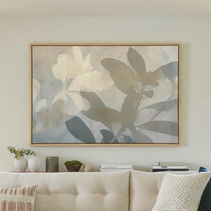 May include: A large rectangular framed wall art piece featuring an abstract botanical print in muted shades of beige, gray, and soft blue. The artwork displays layered leaf silhouettes and floral shapes, encased in a light-toned wooden frame.