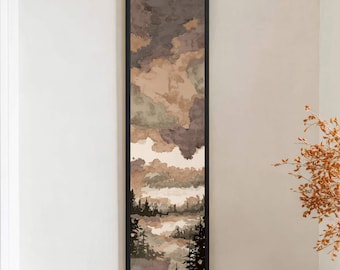 May include: A long, vertical framed art piece with a landscape scene. The artwork features a forest silhouette at the bottom, with layered clouds in shades of brown, beige, and green. The frame is black, and the artwork is displayed on a white wall.