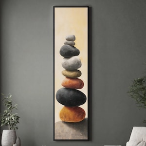 May include: A vertical framed artwork featuring a stack of smooth, colorful stones. The stones range in color from black and gray to orange and yellow, set against a light yellow background. The artwork is displayed in a modern living room setting.