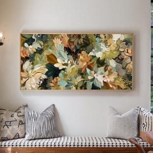 May include: A floral painting in a gold frame, featuring a mix of white, green, and brown flowers. The artwork hangs above a bench with patterned pillows. The painting's colors and textures create a natural, artistic aesthetic.