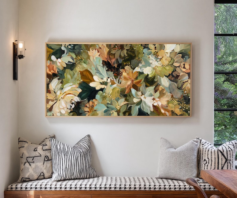 May include: A floral painting in a gold frame, featuring a mix of white, green, and brown flowers. The artwork hangs above a bench with patterned pillows. The painting's colors and textures create a natural, artistic aesthetic.