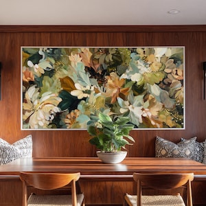 May include: A large floral painting in a white frame hangs above a wooden dining table. The artwork features a mix of white, green, and tan flowers. A small potted plant sits on the table. Two wooden chairs are in front of the table.