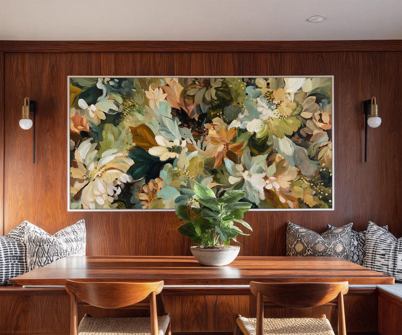 May include: A large floral painting in a white frame hangs above a wooden dining table. The artwork features a mix of white, green, and tan flowers. A small potted plant sits on the table. Two wooden chairs are in front of the table.