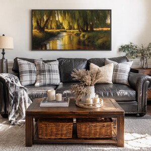 May include: A living room scene featuring a dark leather sofa with plaid pillows and a throw blanket. A wooden coffee table holds candles, books, and a tray with dried flowers. A framed landscape painting hangs above the sofa.