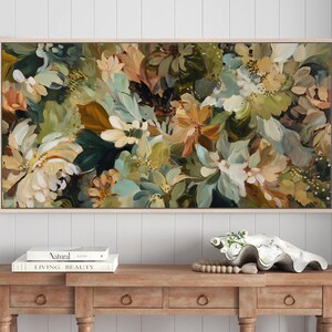 May include: A rectangular floral painting in a light wood frame. The artwork features a dense arrangement of flowers in shades of white, green, brown, and peach. The painting is displayed above a wooden console table with books and decorative items.