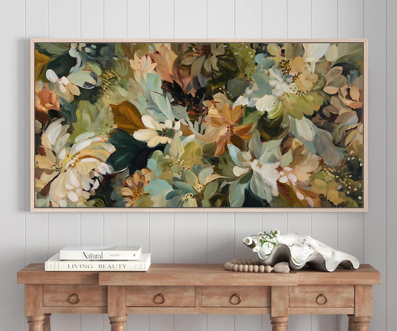 May include: A rectangular floral painting in a light wood frame. The artwork features a dense arrangement of flowers in shades of white, green, brown, and peach. The painting is displayed above a wooden console table with books and decorative items.