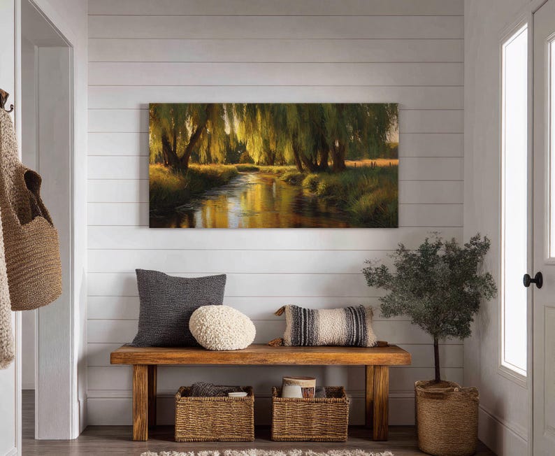 May include: A rectangular landscape painting depicts a serene river scene with weeping willow trees. A wooden bench with pillows and baskets sits below the artwork. A small potted tree is next to the bench.