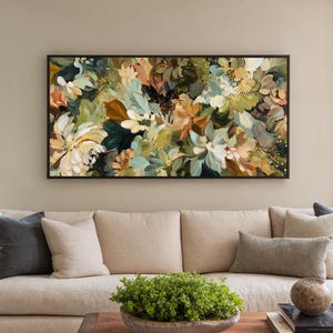 May include: Abstract floral painting in a black frame. The artwork features a mix of white, green, and orange flowers. The painting hangs above a beige sofa with pillows.