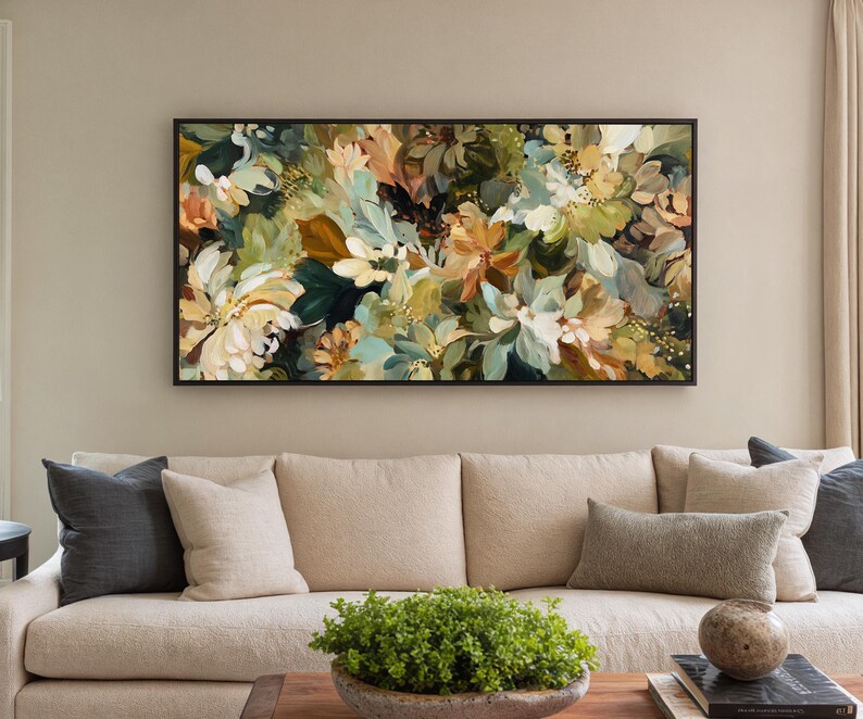 May include: Abstract floral painting in a black frame. The artwork features a mix of white, green, and orange flowers. The painting hangs above a beige sofa with pillows.