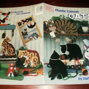 May include: A craft instruction booklet titled Plastic Canvas CATS by Darla J. Fanton and produced by Jean Leinhauser. The cover features various cat-themed plastic canvas projects, including wall hangings, tissue box covers, and figurines.